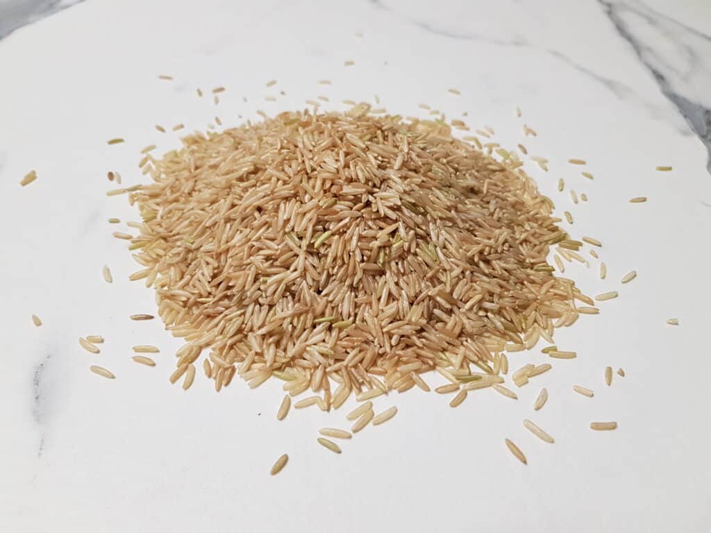 Raw brown basmati rice on a white marble worktop.