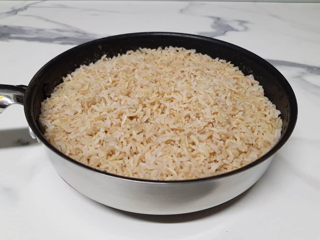 Brown basmati rice in a non-stick pan on a white marble worktop.