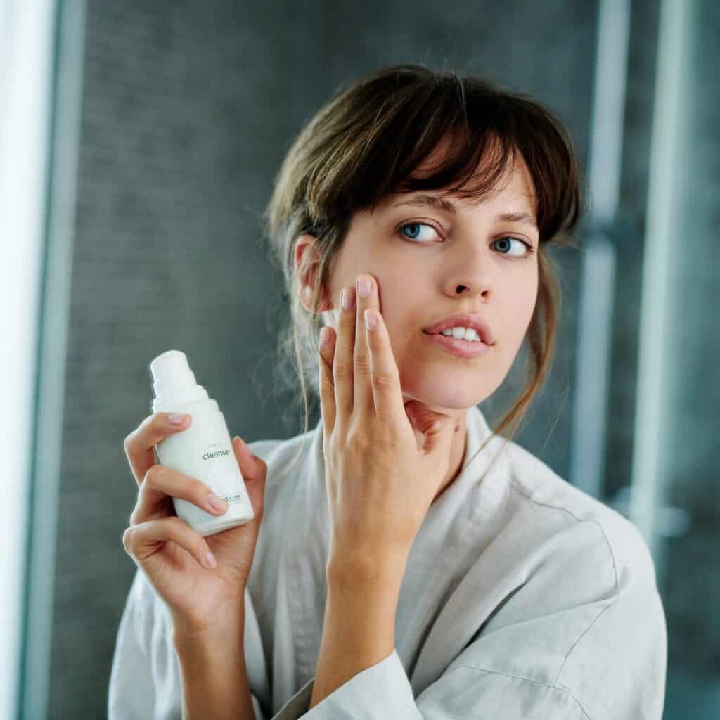 A model holding a bottle of Ringana fresh vegan cleanser in front of a mirror.