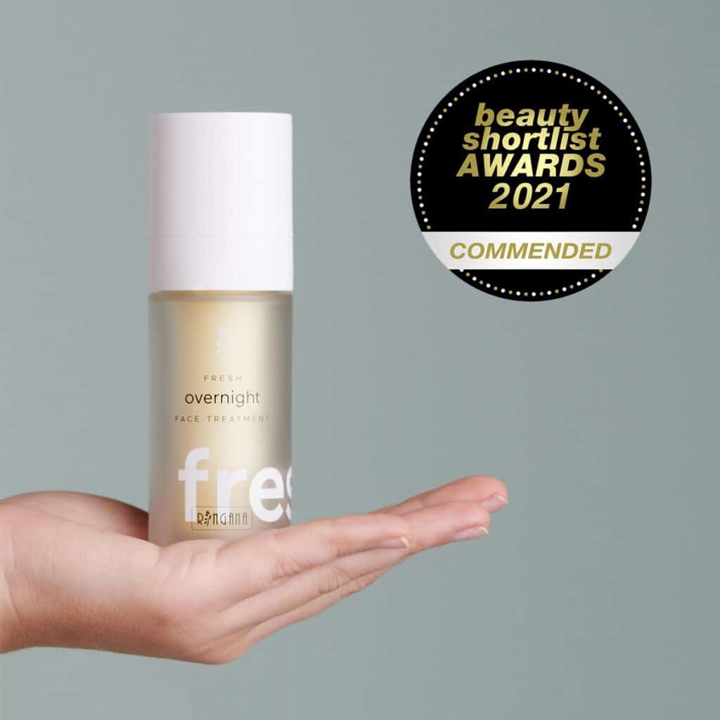 A hand holding a bottle of Ringana Overnight face treatment with an award lable