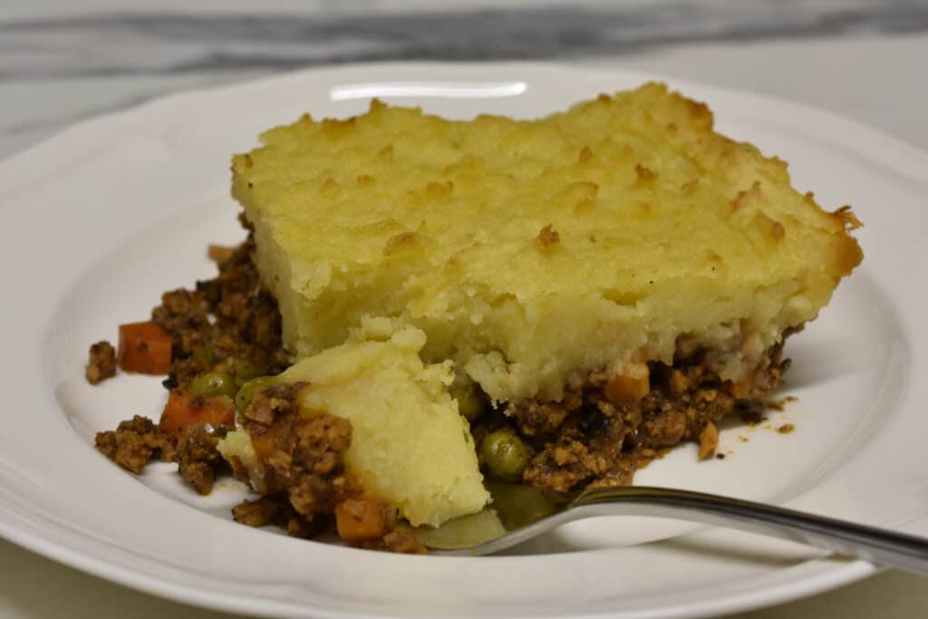 Close up image of vegan shepherd's pie on a white plate with a fork