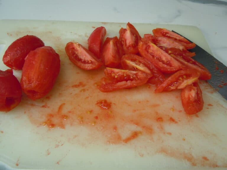 Skinned and quartered Italian plum tomatoes on a white chopping board