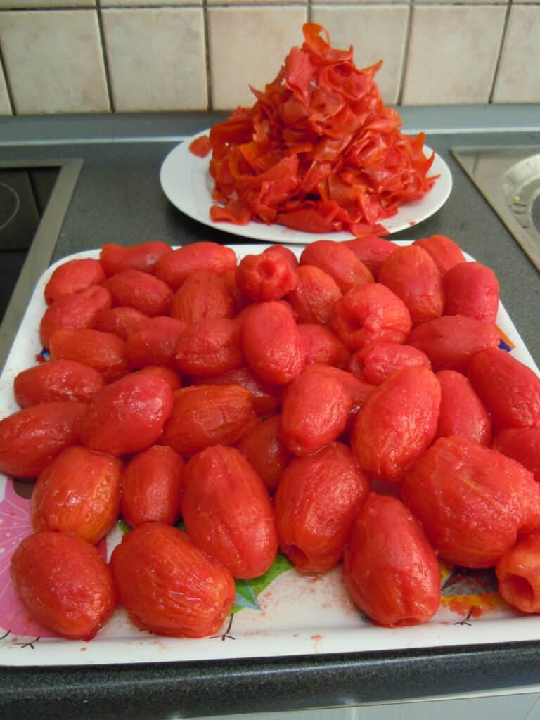 Skinned Italian plum tomatoes on a white tray, with the discarded skins in the background