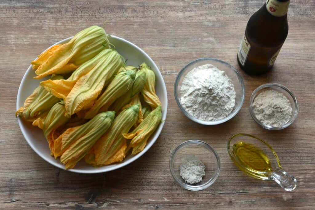 Ingredients for beer-battered courgette (zucchini) flowers on a wooden table.