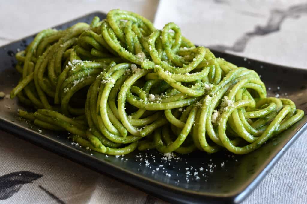 Spaghetti with vegan basil pesto and vegan Parmesan cheese on a black plate