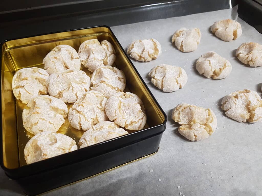 Vegan almond biscuits in a metal biscuit tin and on a baking tray