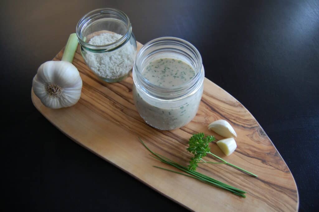 Vegan cashew cream cheese with garlic and chives in a glass jar on a wooden board with ingredients