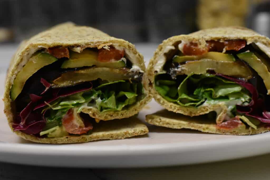 Vegan piadina wraps with grilled vegetables, tomatoes, salad, hummus, and vegan mayonnaise on a plate