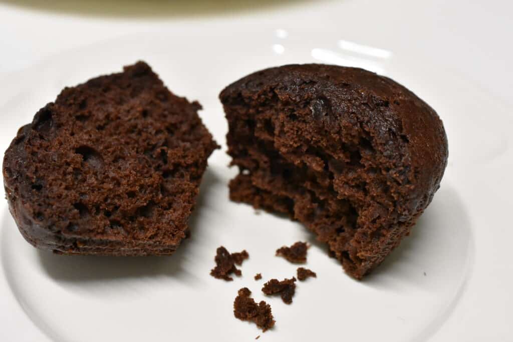 Close up of a vegan cholate muffin broken in half on white plate