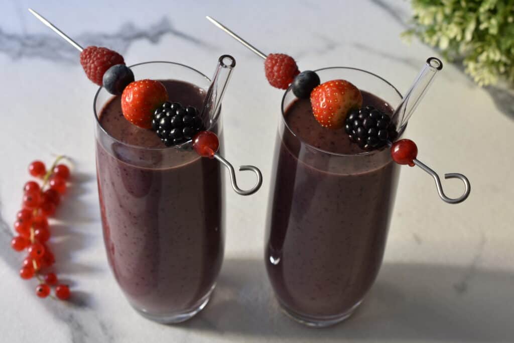 Mixed berry superfood breakfast smoothies with skewers with fruit on then on a kitchen worktop