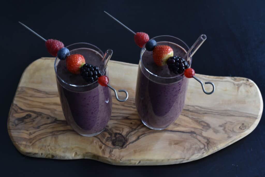 Mixed berry superfood smoothies in glasses with skewers with berries on them, on a wooden board