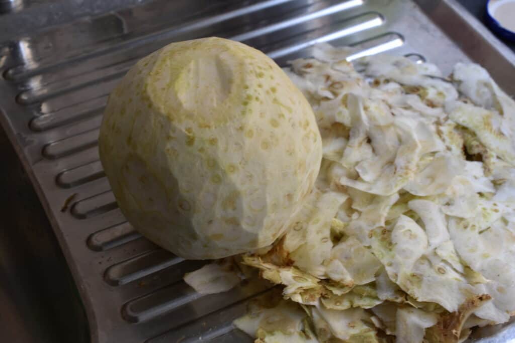 A whole peeled celeriac, on a kitchen draining board with the peelings on the right