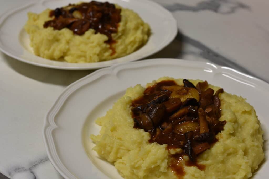 2 plates of mushroom bourguignon and mashed potato on white plates on a kitchen counter