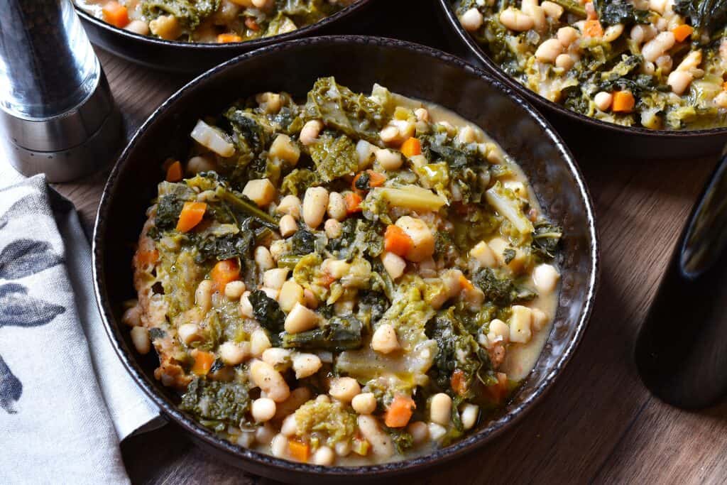 Three bowls of Tuscan ribollita on a wooden table.