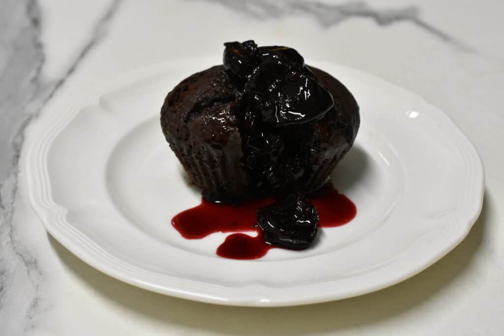 Vegan chocolate muffin with hot cherry sauce on a white plate