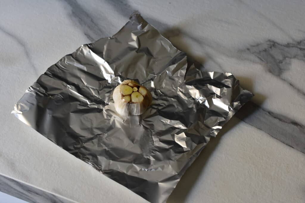 A head of garlic with the top part sliced off, on a sheet of aluminium foil