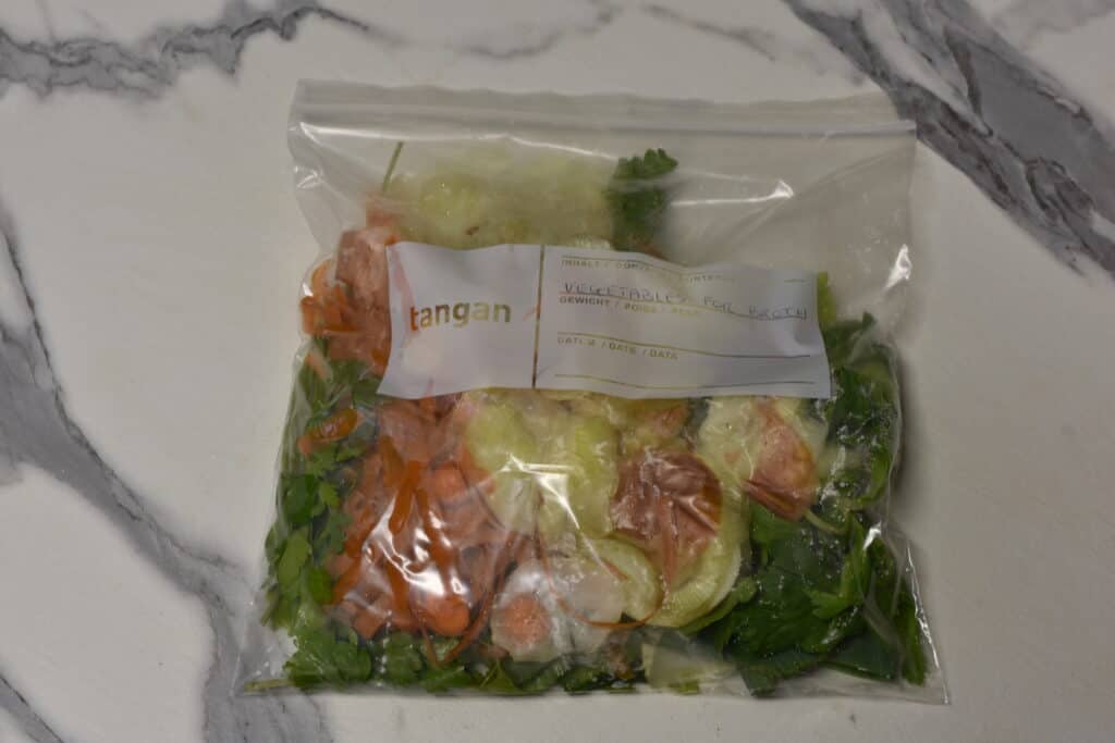 A freezer bag full of vegetable scraps for making broth on a kitchen worktop.