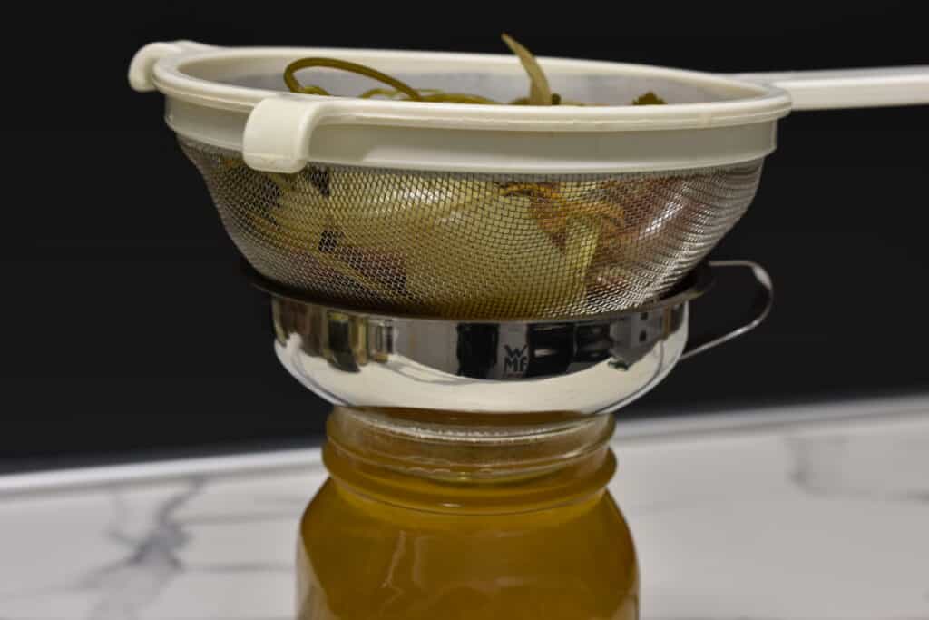 Straining vegetable broth through a sieve into a jar.