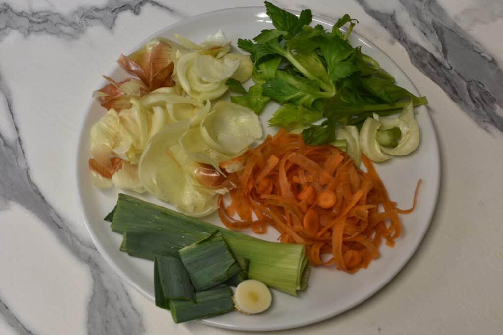 Vegetable scraps for broth (onion, carrot, celery and leek) on a plate.