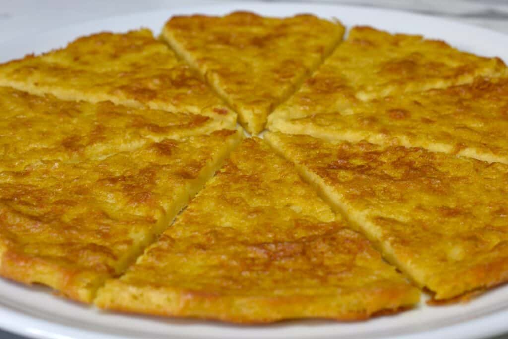 A close-up image of a whole farinata cut into eight slices on a white plate,