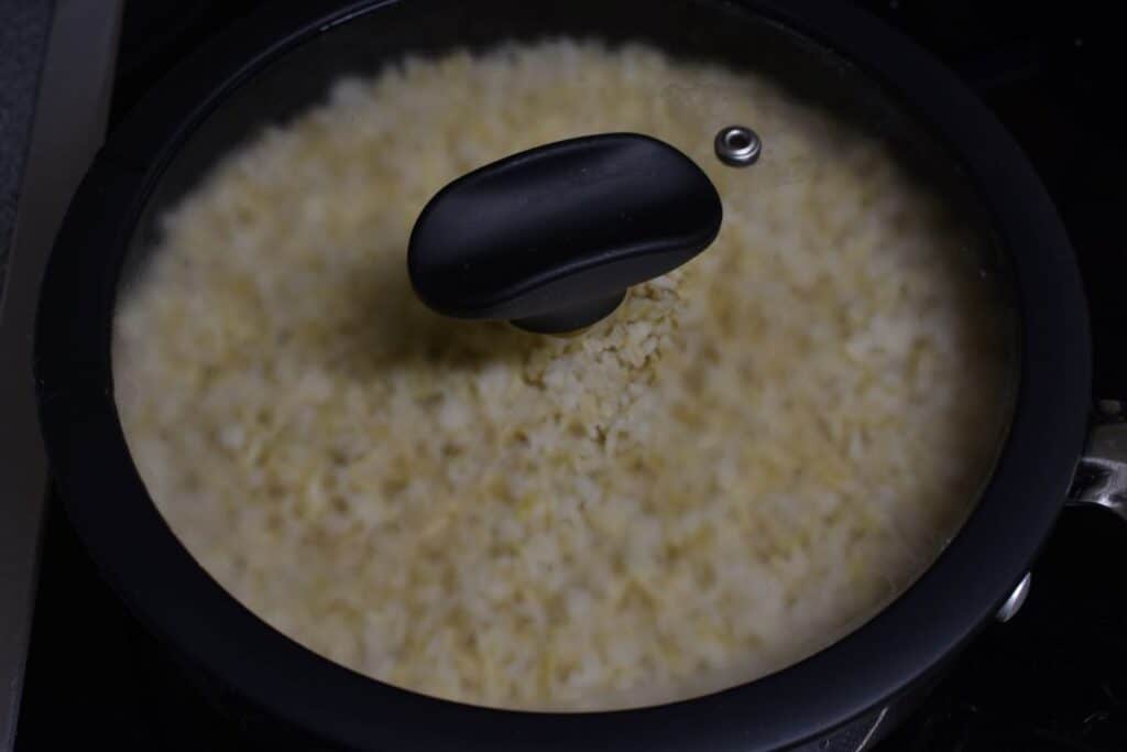 Brown basmati rice steam cooking on a stovetop in a pan with a glass lid.