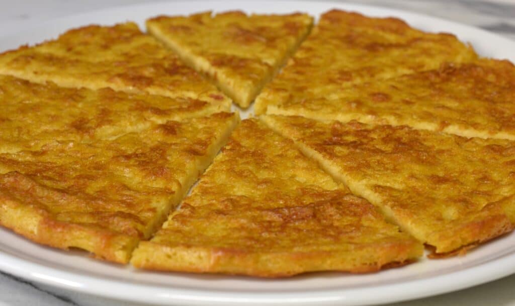 A close-up image of a whole farinata cut into slices on a white plate