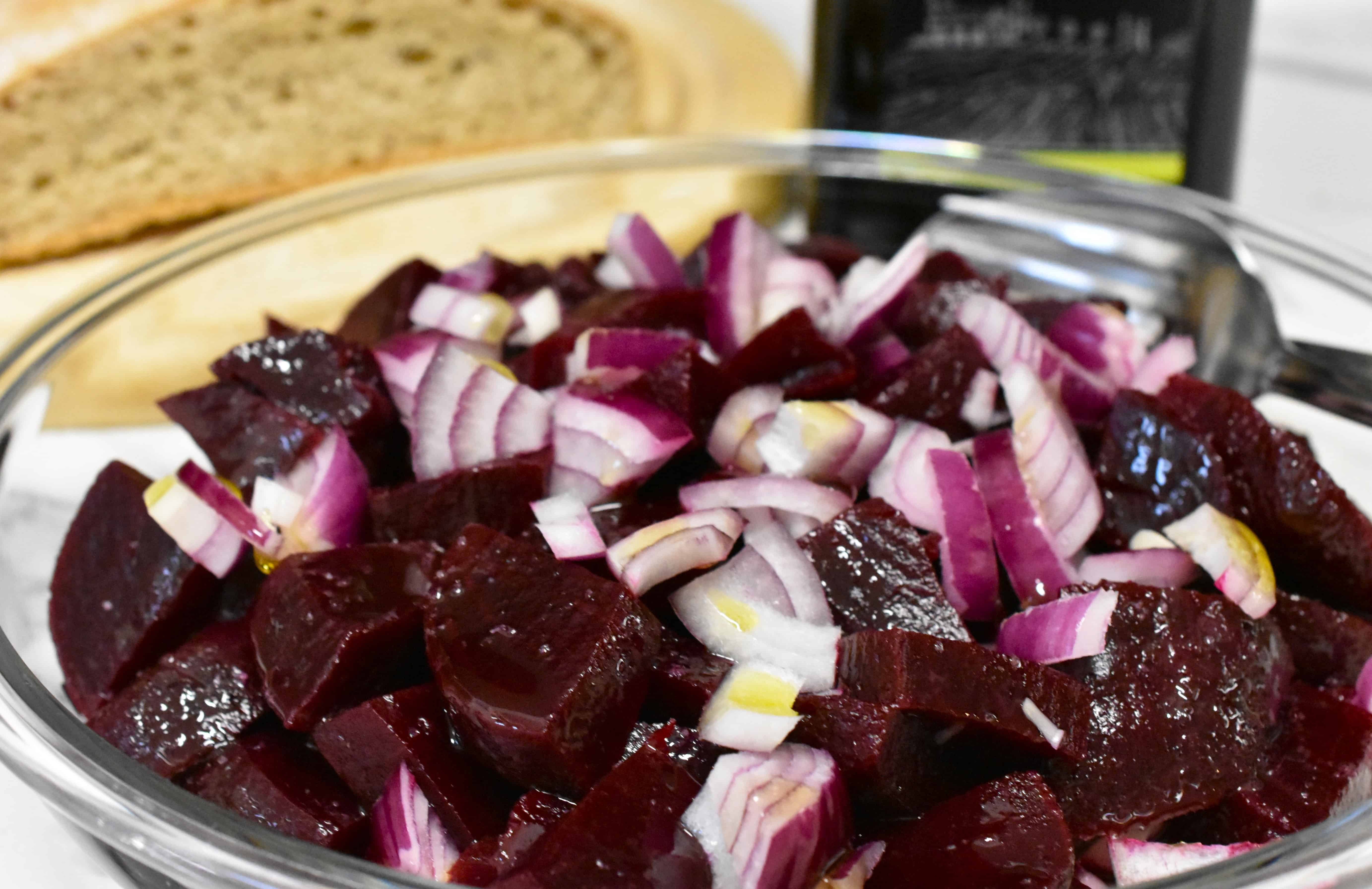 A close-up image of simple beetroot salad in glass bowl with a serving spoon and fork.