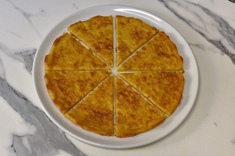 A whole farinata cut into slices on a white plate