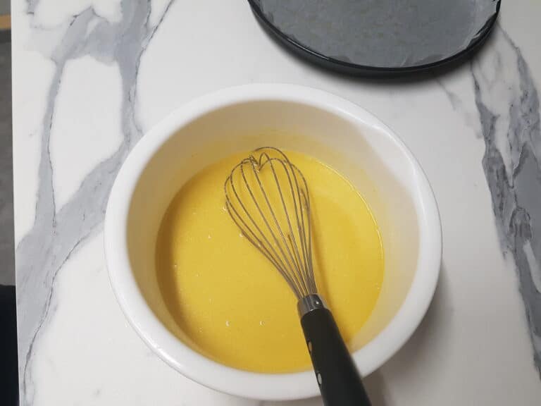 Chickpea farinata batter in a white bowl with a hand whisk