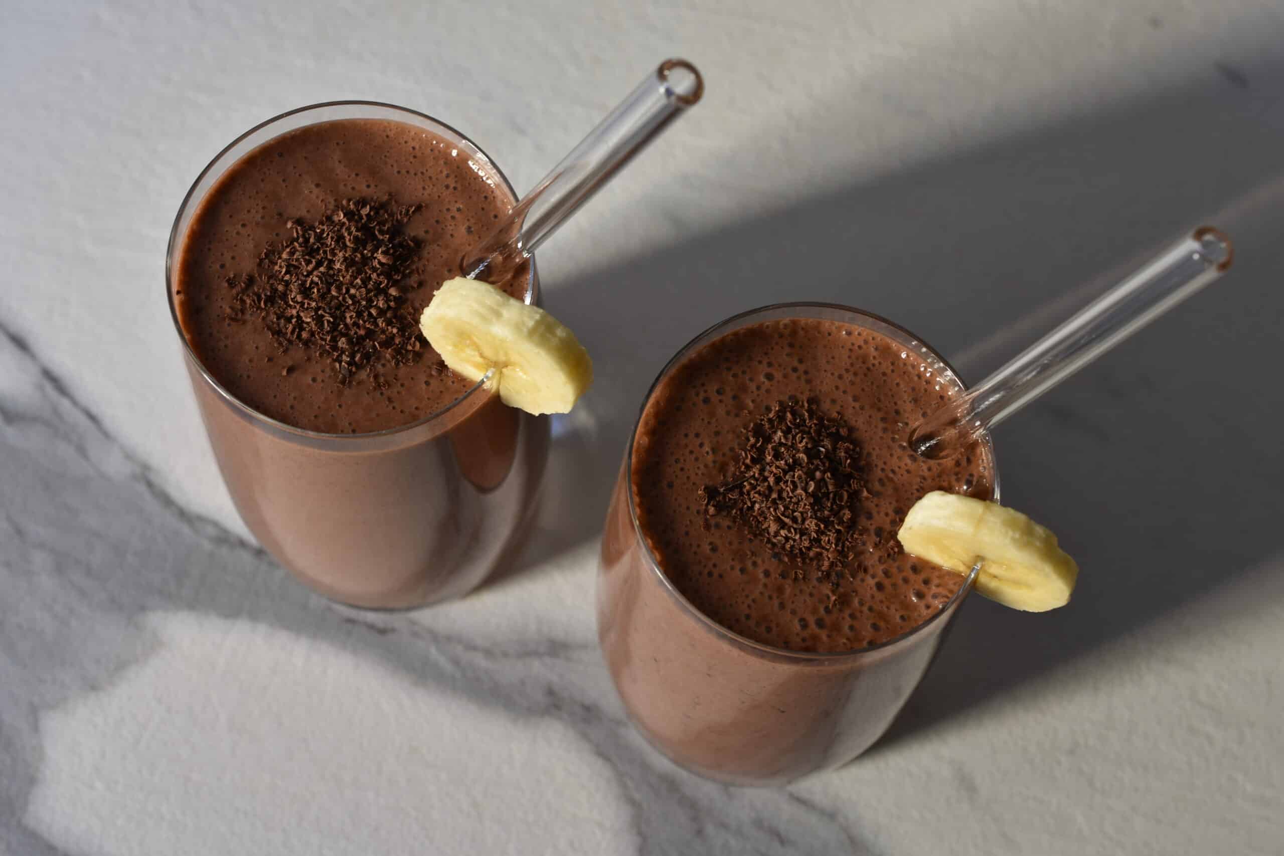 Two glasses of chocolate banana protein shake on a kitchen worktop