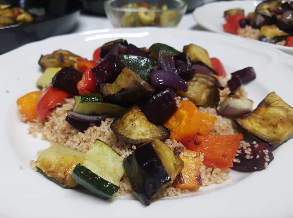 A close-up image of roasted vegetable couscous on a white plate.