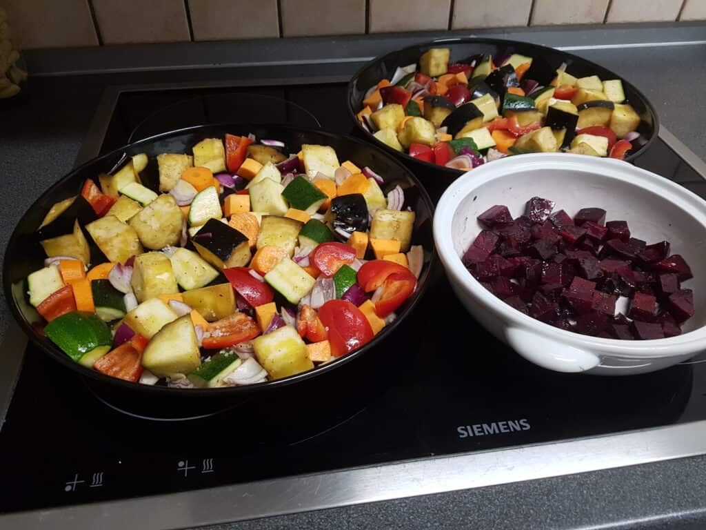 Cubes of raw vegetables tossed in olive oil in tart tins before roasting.