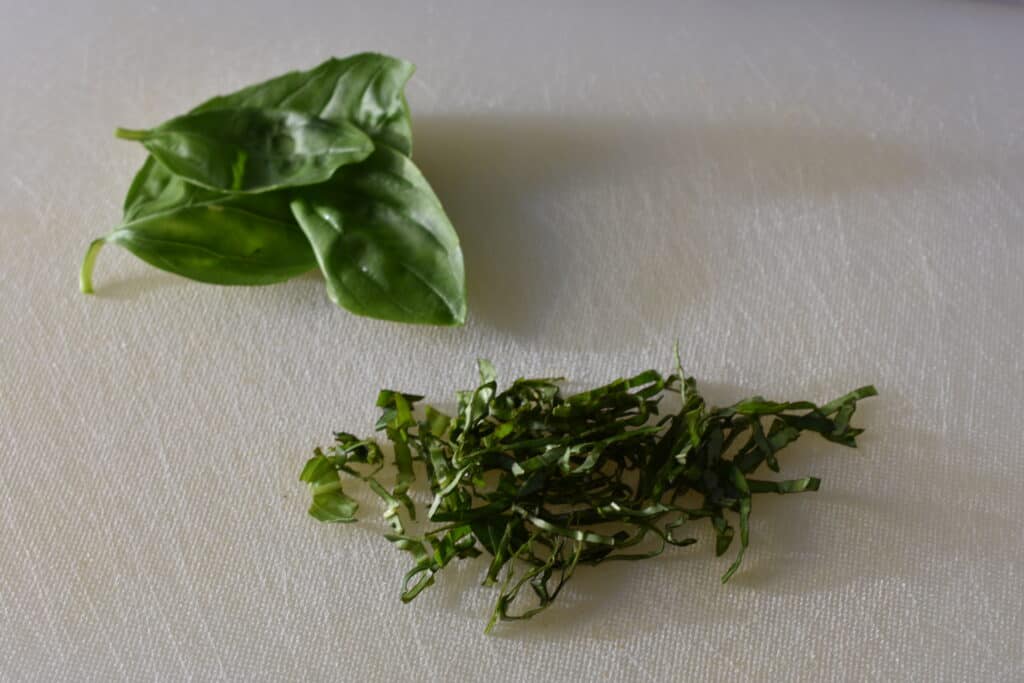 Three fresh basil leaves and basil julienne on a white chopping board