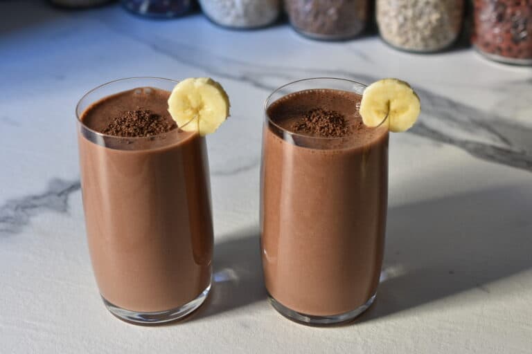 Vegan chocolate banana protein shake with dark vegan chocolate shavings and slices of banana.