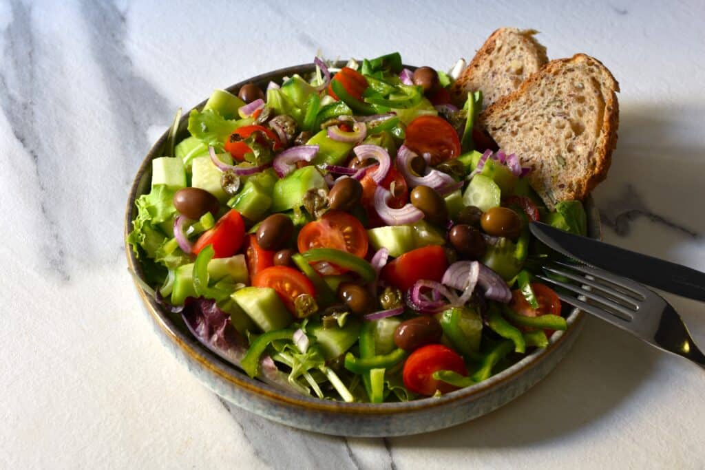 Greek-style mixed salad on a grey plate with 2 slices of sourdough bread