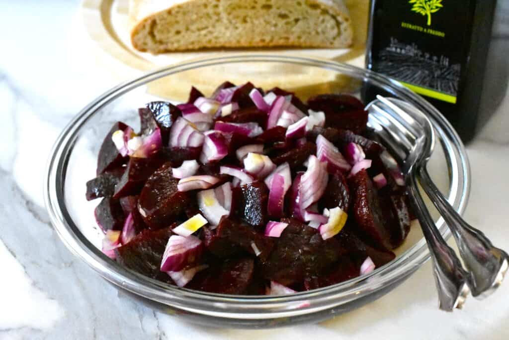 Simple beetroot salad in a glass bowl with a serving spoon and fork.