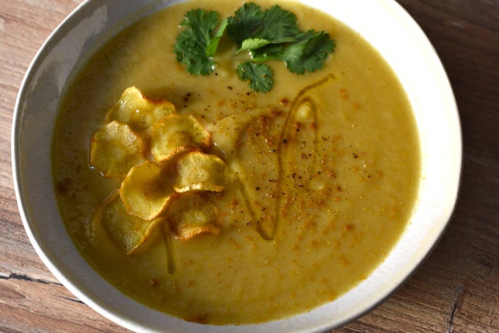 Spicy parsnip soup with a garnish of parsnip chip, ground cumin and green coriander leaf.