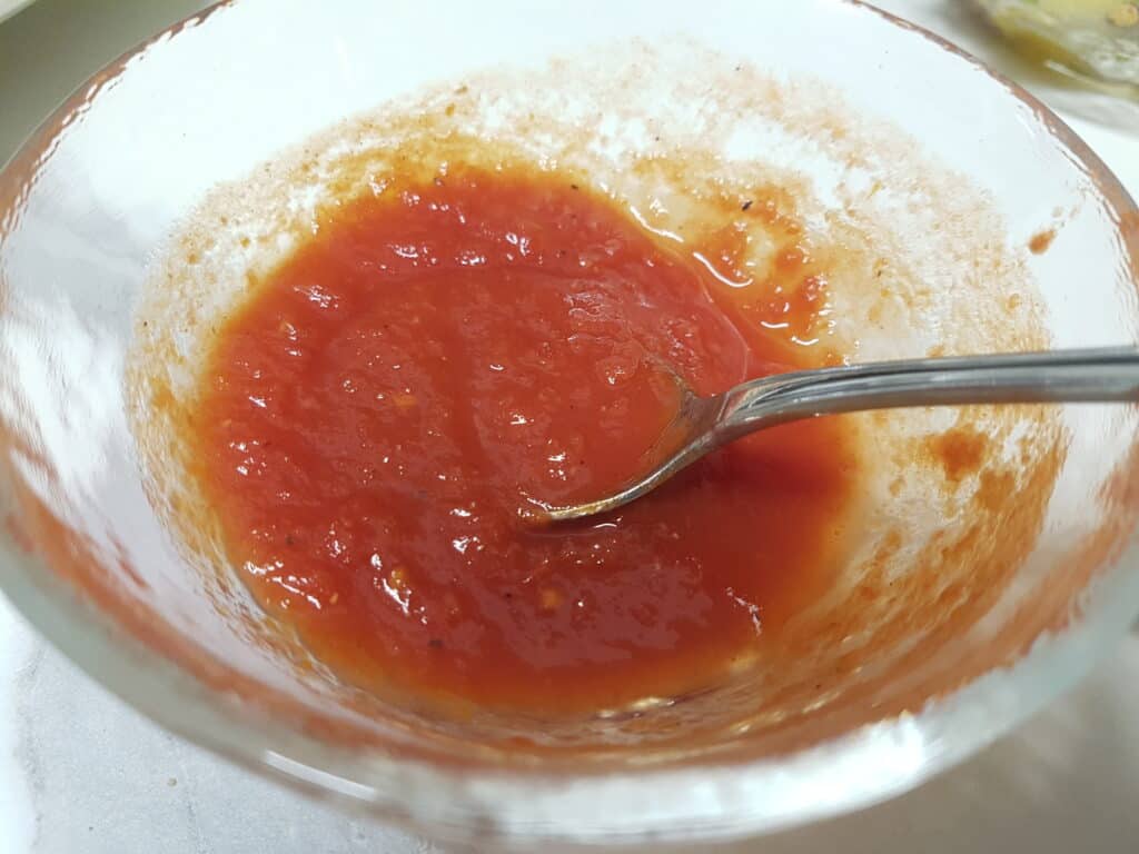 Sweet and sour tomato sauce for roasted vegetable couscous in a glass bowl with a spoon.