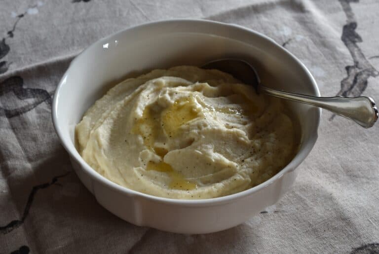 Creamy vegan celeriac mash in a white serving bowl with a spoon