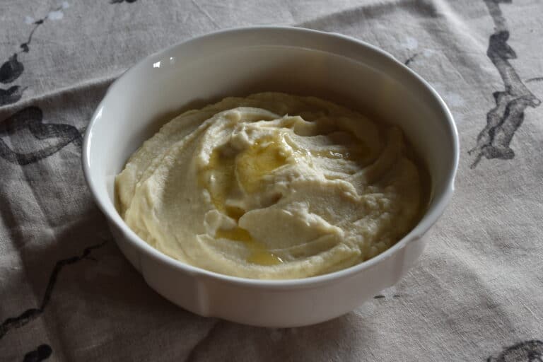 Creamy vegan celeriac mash with melted butter in a white serving bowl