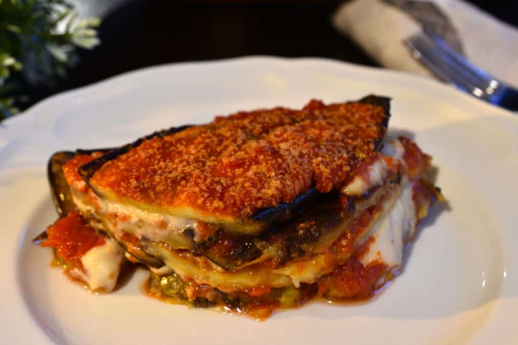 A piece of vegan aubergine parmigiana on a white plate.