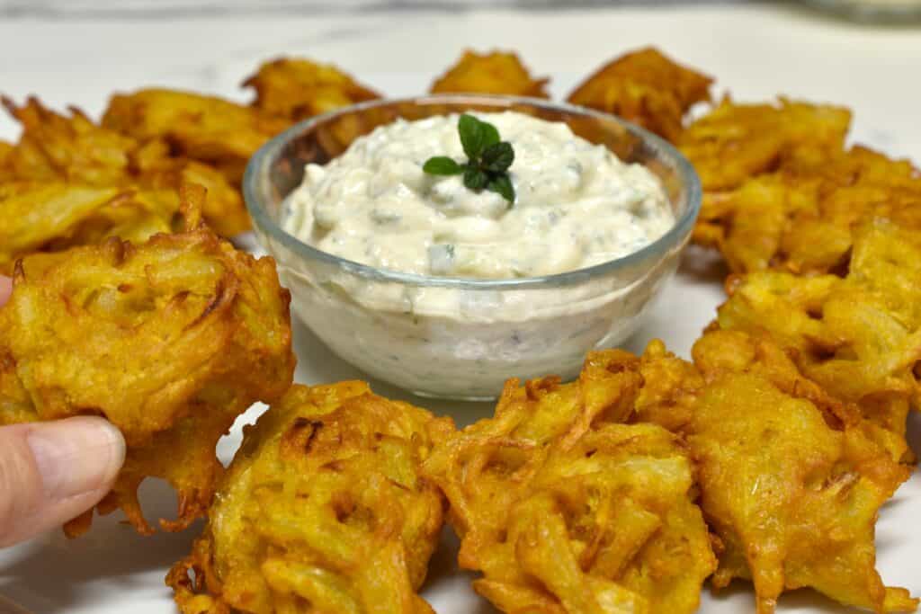 Onion bhaji and cucumber mint raita with a hand holding an onion bhaji