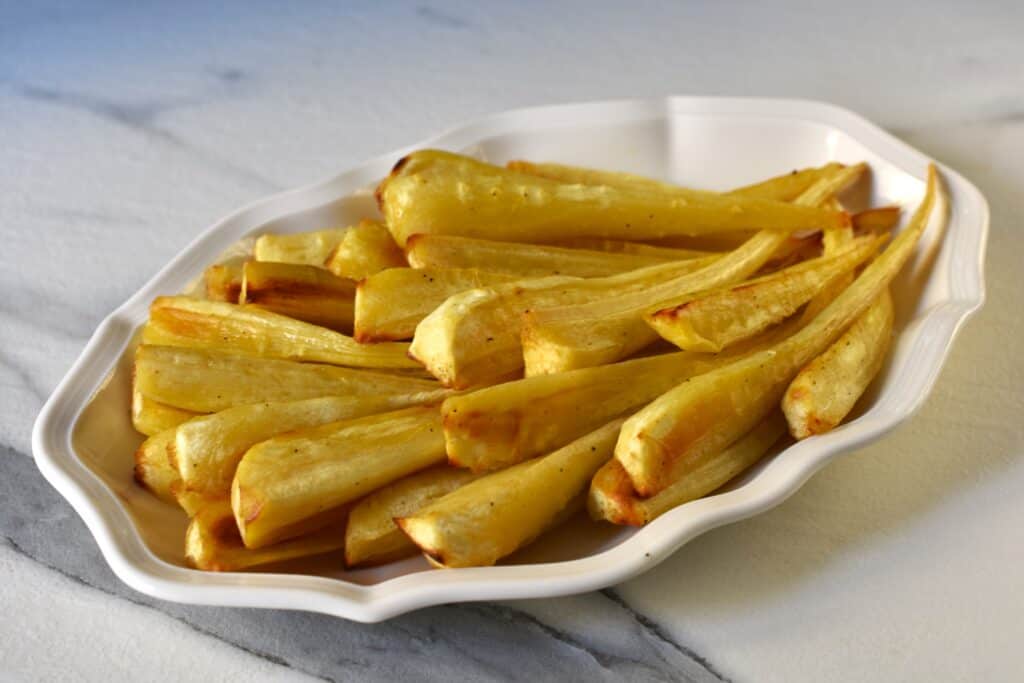 Oven-roasted parsnips on a white serving plate on a kitchen worktop