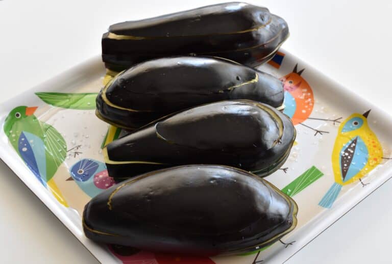 Four aubergines being salted on a tray on a kitchen worktop