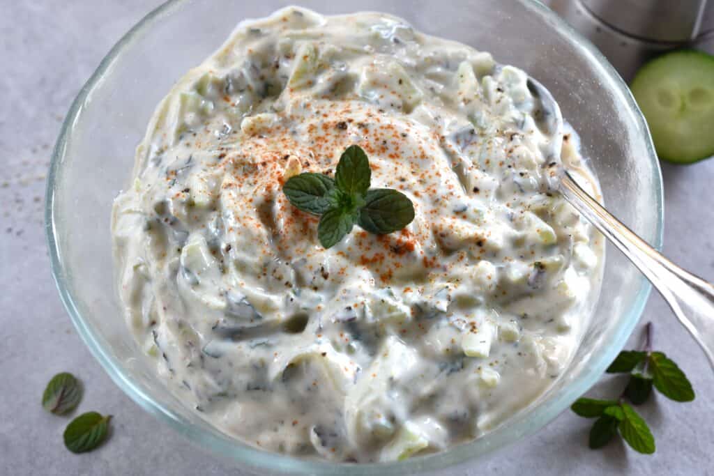 Vegan cucumber raita in a glass bowl with a spoon and a garnish of mint