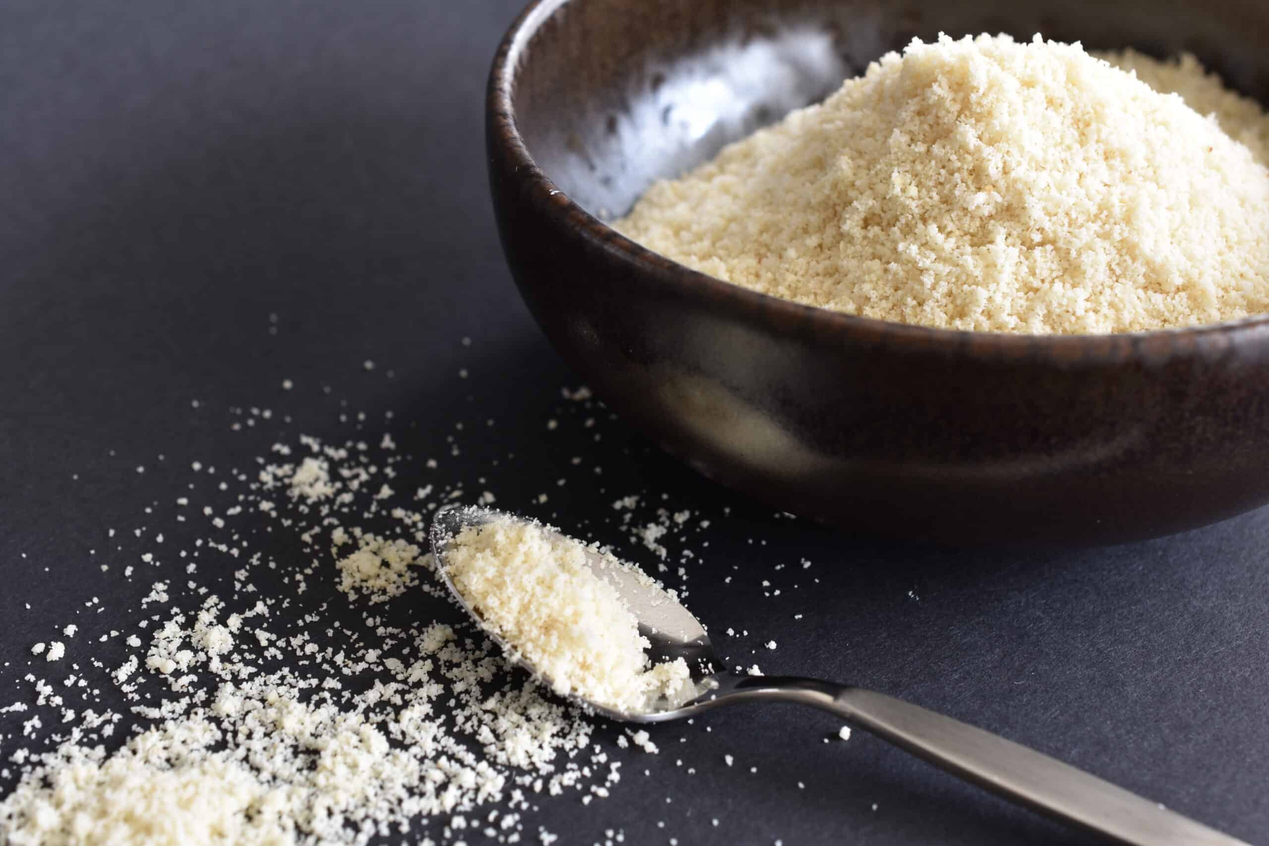 Vegan parmesan cheese in a brown bowl with a spoon and cheese in the foreground