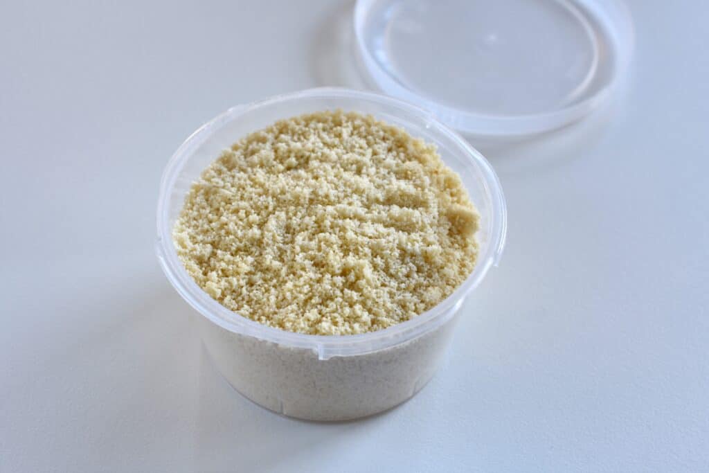 Vegan parmesan cheese in a plastic container with a lid on a kitchen worktop.