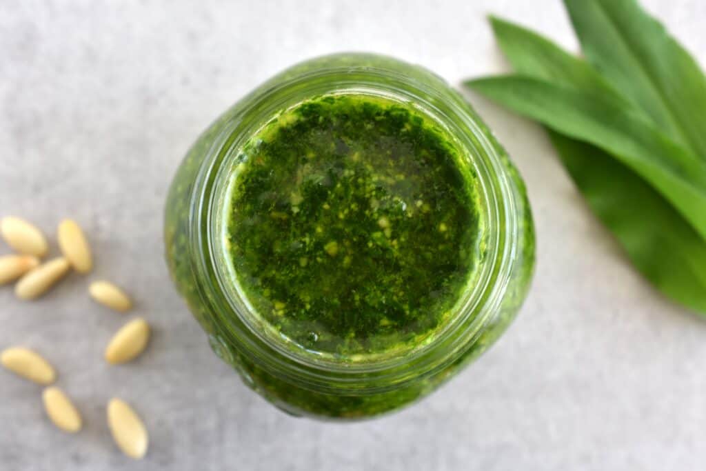 Wild garlic pesto in a jar with some wild garlic leaves and pine nuts