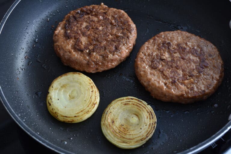 Cooked vegan fast food burgers and onion slices in a frying pan.