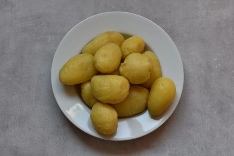 Potatoes boiled in their skins and then peeled, on a white plate.